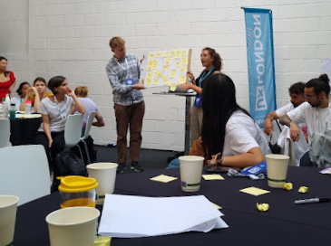 Two people presenting a board with sticky notes to other participants in a workshop at UX London 2022